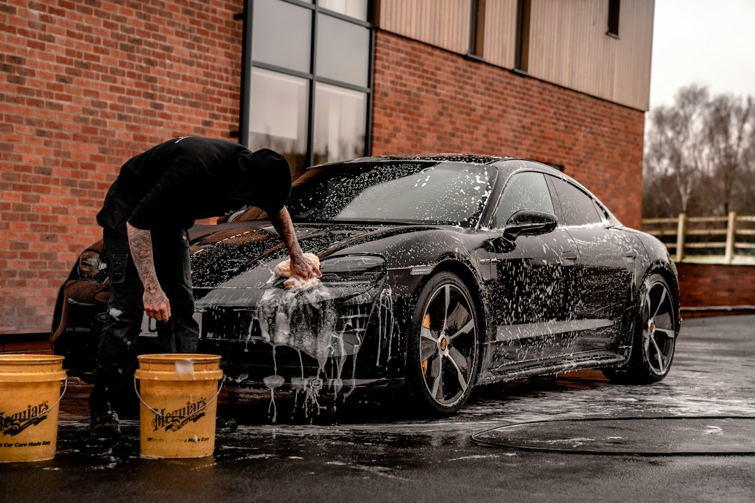 A worker washing a black car with water outdoors